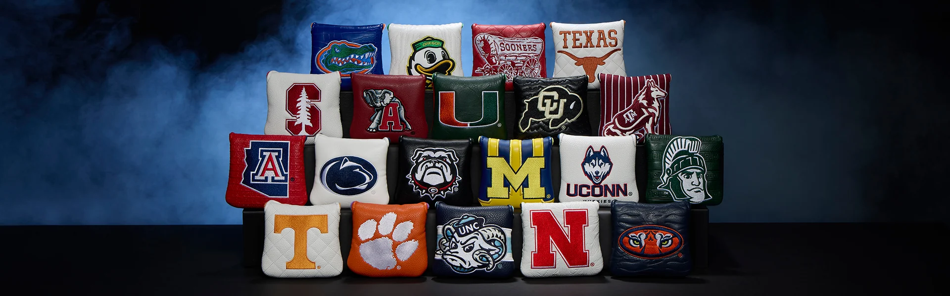 TaylorMade collegiate team putter headcovers on a smoky blue backdrop